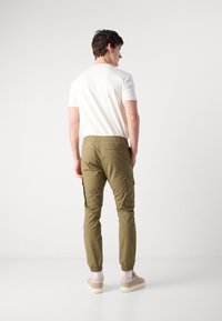 Khaki cargobroek met een elastische tailleband en enkelsluiting, voorzien van zijzakken en een zachte katoenen mix. G gedragen met een wit t-shirt.