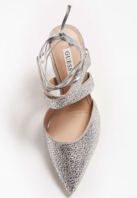 Chaussure à talon haut argentée avec un bout pointu, ornée de strass, dotée de brides croisées et d'un lien fin autour de la cheville. Doublure intérieure lisse.