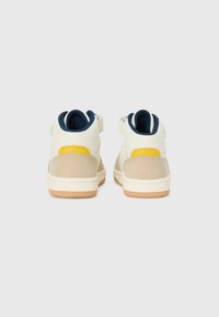 Baskets montantes avec une tige en cuir blanc, des accents en daim beige, une languette de talon jaune et une doublure bleu marine. Semelle en caoutchouc pour une meilleure traction.