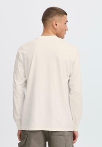 Camiseta de algodón beige de manga larga con un escote redondo y un corte relajado. La tela parece suave, con un estiramiento mínimo y sin patrones visibles.