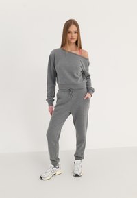 Hallide hallide ja puuvillasegusest jumpsuit, millel on madalad õlalõiked, elastne vöökoht ja tõmblukk. Ühendatud valgelt treeningjalatsitega.