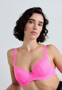 Rosefarbenes Spitzen-BH mit gewelltem Saum, Unterdrahtunterstützung und dekorativen Verzierungen in der Mitte. Verstellbare Träger für die perfekte Passform.