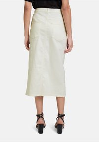 Jupe midi en denim beige clair avec une coupe droite, des poches arrière et des coutures visibles, associée à des talons noirs à brides.