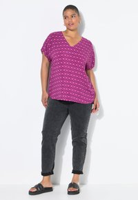 Top de manga corta en fucsia vibrante con escote en V y patrón de diamantes. Combinado con jeans ajustados negros y sandalias negras tipo slide.