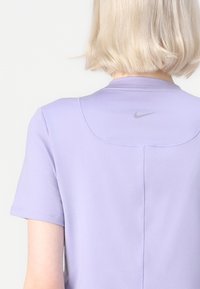 Světlofialové sportovní tričko Nike s krátkými rukávy, kulatým výstřihem a malým stříbrným logem na zadní straně. Hladká textura.