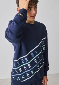 Marineblauer Sweatshirt aus Baumwollmischung mit weißem und minzgrünem Textdesign. Verfügt über gerippte Bündchen, einen Rundhalsausschnitt und einen Logoaufnäher auf dem Ärmel.