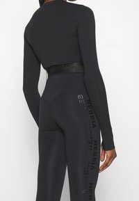 Czarny, długi rękaw, krótki top o dopasowanym kroju i wysokim pasie. Legginsy mają czarne logo nadrukowane pionowo po bokach. Gładka faktura.