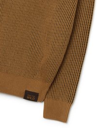 Bruine geribde gebreide trui met een mouw en een manchet, en een klein donker label met de tekst "RIDE THE WILD" dicht bij de zoom.