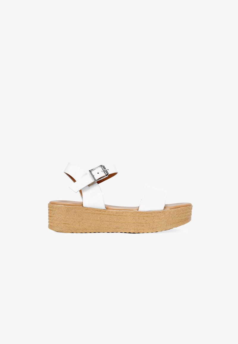 White leather platform sandals with an adjustable ankle strap, cork textured sole, and smooth footbed. Features a simple design and silver buckle.
