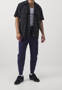 Svart t-shirt med kort ärm och två bröstfickor, vit linne under, lila tapered mjukisbyxor och svarta sneakers med detaljer.