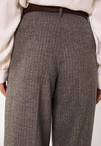 Pantaloni grigi a righe sottili con vita sartoriale, tasche posteriori e un tessuto testurizzato. Abbinati a una blouse di colore chiaro.