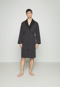 Ciemnoszara szlafrok z szalowym kołnierzem, paskiem w talii i dwoma przednimi kieszeniami. Wykonany z miękkiego materiału o lekko textured wykończeniu.