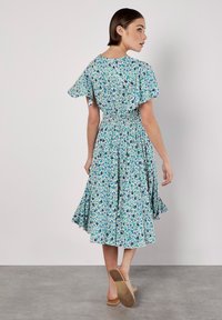 Blumenkleid Midi mit tailliertem Schnitt, ausgestellten Ärmeln und blau-grünen Mustern. Hergestellt aus leichtem Stoff, mit einem fließenden Rock.