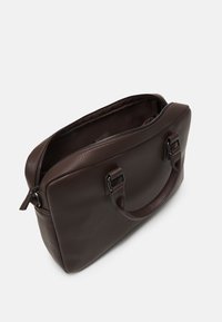 Sac à main en cuir marron avec une finition texturée, deux anses et une fermeture éclair. L'intérieur présente une doublure sombre, sans motifs ni accents visibles.