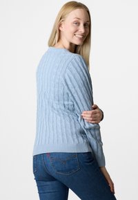 Helles blaues, strukturiertes Strickpullover mit Zopfmuster, rundem Ausschnitt und geripptem Saum, kombiniert mit eng anliegenden Jeans in einer dunkleren Waschung.