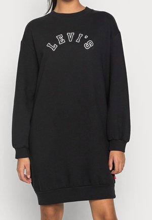 Osoba ubrana w czarną sukienkę typu sweatshirt z długim rękawem, z napisem "LEVI'S" wydrukowanym białymi literami na piersi.