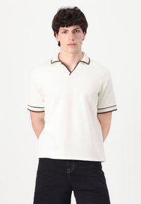 Kortärmad polo-tröja i off-white med V-ringning, brun kant vid kragen och ärmarna, ribbad textur och avslappnad passform.