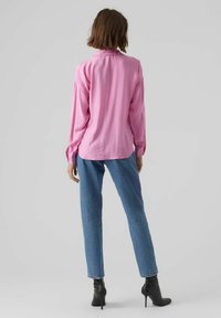 Różowa koszula z długim rękawem o luźnym kroju, w połączeniu z jasnoniebieskimi spodniami z wysokim stanem i czarnymi botkami do kostek. Prosty, jednolity wzór.