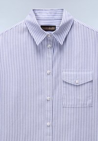 Light blue and white striped button-up shirt with a collar, front pocket, and white buttons. Fabric appears smooth with a slight texture.