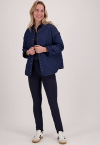 Gequilted marineblauwe jas met drukknoopsluiting, met een relaxte pasvorm en contrasterende manchetten, gecombineerd met marineblauwe leggings en witte sneakers.