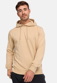 Beige hoodie met een trekkoord, ribgebreide manchetten en zoom. Bevat een klein logo op de borst, gemaakt van zacht materiaal. Lange mouwen.