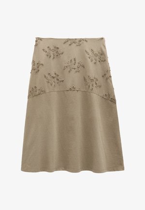 Beżowa spódnica w kształcie litery A z wypukłą haftowaną górną połową z motywem kwiatowym i gładkim materiałem na dolnej połowie.