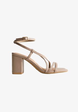 Beige sandaal met hoge hak en blokhak, dunne gekruiste bandjes over de tenen, en verstelbare enkelband met gesp.