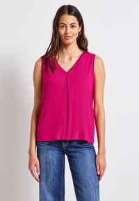 Top fucsia senza maniche con scollatura a V e dettaglio di cuciture verticali, realizzato in tessuto morbido; abbinato a jeans in denim chiaro.
