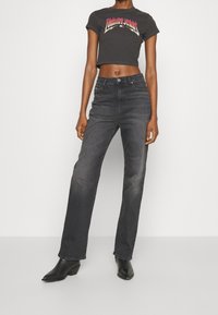 Černé zkrácené tričko s potiskem "Tommy Jeans", spárované s tmavě šedými volnými džíny a černými botami na podpatku. Jednoduchý design, přiléhavý vršek.