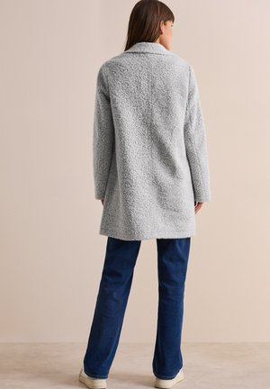 Grå, texturerad kappa med krage och långa ärmar, bärs över mörkblå, raka byxor. Kappan har en lös passform och medellång design.