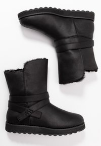 Schwarze Leder-Ankle Boots mit strukturierter Oberfläche, Kunstfellfutter und einem umlaufenden Riemen. Die Sohle ist dick und hat einen wellenförmigen Rand.
