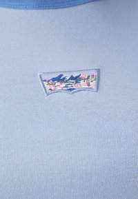 Top in tessuto blu chiaro a coste con scollatura rotonda. Presenta un'patch ricamata che raffigura montagne e fiori.
