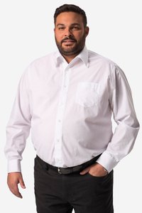 Mand med skæg iført hvid skjorte med knapper og sorte bukser, står med den ene hånd i lommen mod en ensfarvet baggrund.