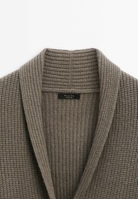 Cardigan en maille taupe avec un large col châle et une texture côtelée, avec une étiquette noire à l'intérieur de l'encolure.