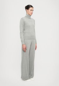 Hellegrauer Strickrollkragenpullover mit Rippenstruktur, kombiniert mit weit geschnittenen passenden Hosen, die beide ein weiches Stoffgefühl haben.