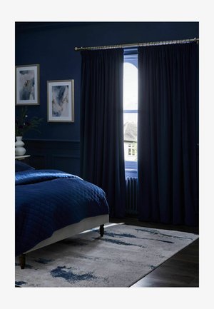 Dunkelblaues Schlafzimmer mit gesteppter Bettdecke, schweren Vorhängen, die am Fenster teilweise geöffnet sind, abstrakter Wandkunst, einer weißen Vase mit Blumen und einem blau gemusterten Teppich.