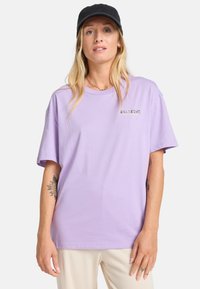 Lavender farvet bomulds t-shirt med korte ærmer og rund halsudskæring. Har et lille, gyldent "BILLABONG" logo på brystet. Glat tekstur.