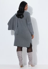 Vestido de punto gris con un corte relajado y mangas estilo capa, con aberturas laterales. Combinado con botas de ante gris hasta la rodilla.