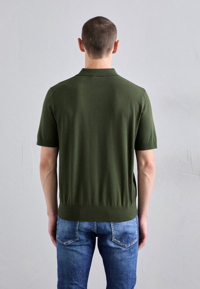 Cămașă polo scurtă de culoare verde închis, confecționată dintr-un material moale. Are un guler și o tiv ribbit. Asortată cu blugi din denim de culoare albastru deschis.