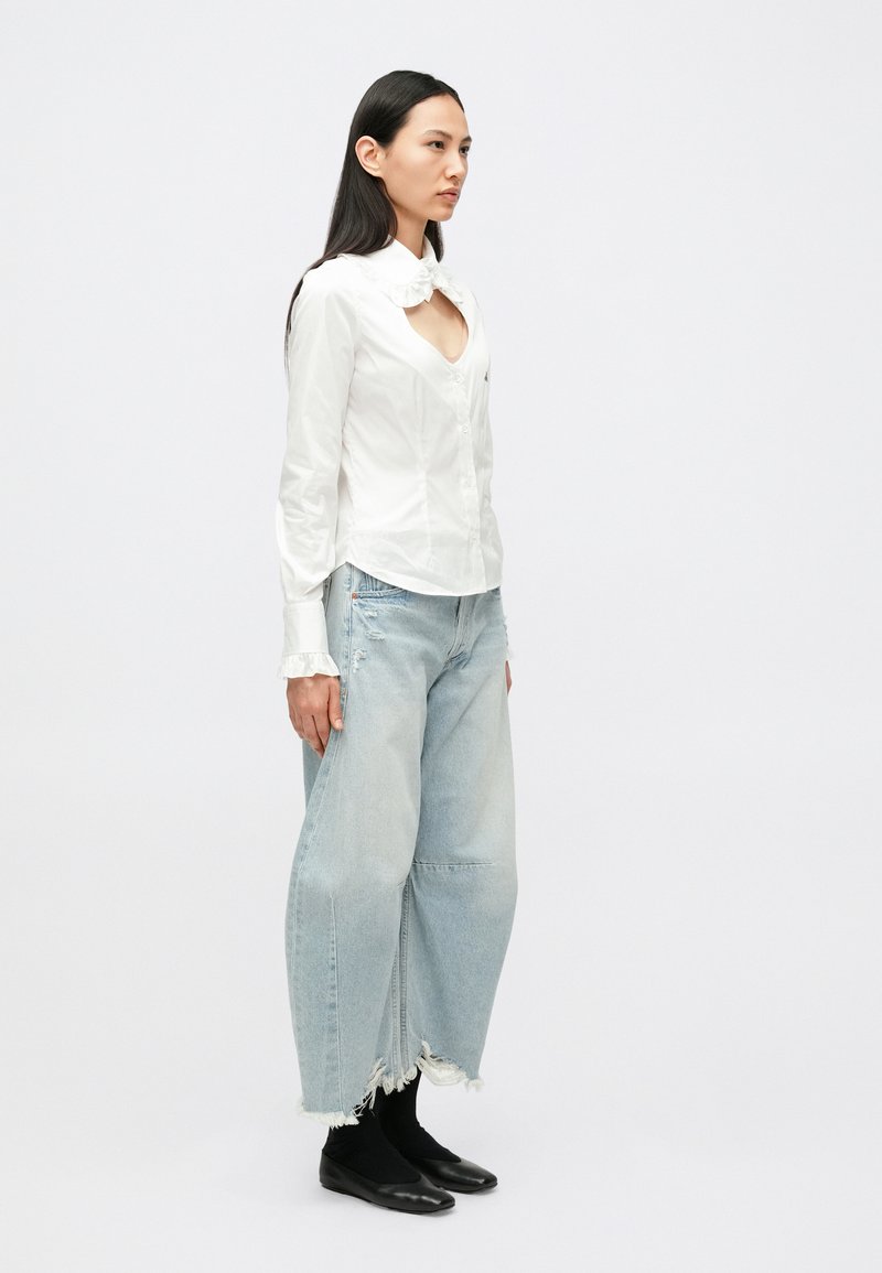 Vit skjorta med knappar och volangkrage, kombinerad med ljusblå, vida jeans med sliten fåll och svarta flata skor.