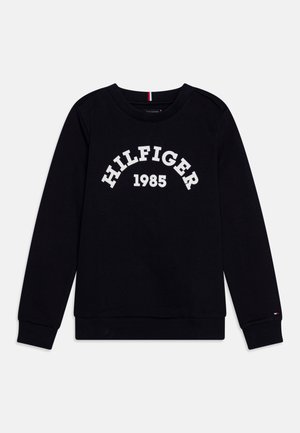 Sort sweatshirtt med lange ærmer og rund hals med "HILFIGER 1985" trykt i hvidt over brystet og lille logo på venstre ærmekant.