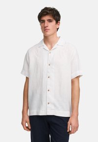 Camisa de lino blanca de manga corta con cuello, botones en la parte delantera y botones de madera natural. Presenta un corte relajado y una textura sutil.
