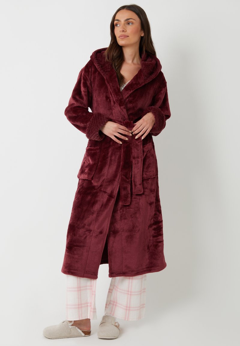 Ropa Marlene en burdeos profundo, hecha de un suave tejido de felpa, con capucha, mangas largas y dos bolsillos frontales. Acompañada de pantalones a cuadros.