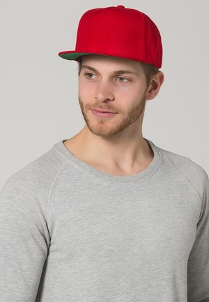 Căciulă roșie de baseball cu brim plat și interior verde, împerecheată cu un tricou lung gri deschis cu guler rotund și mâneci raglan.