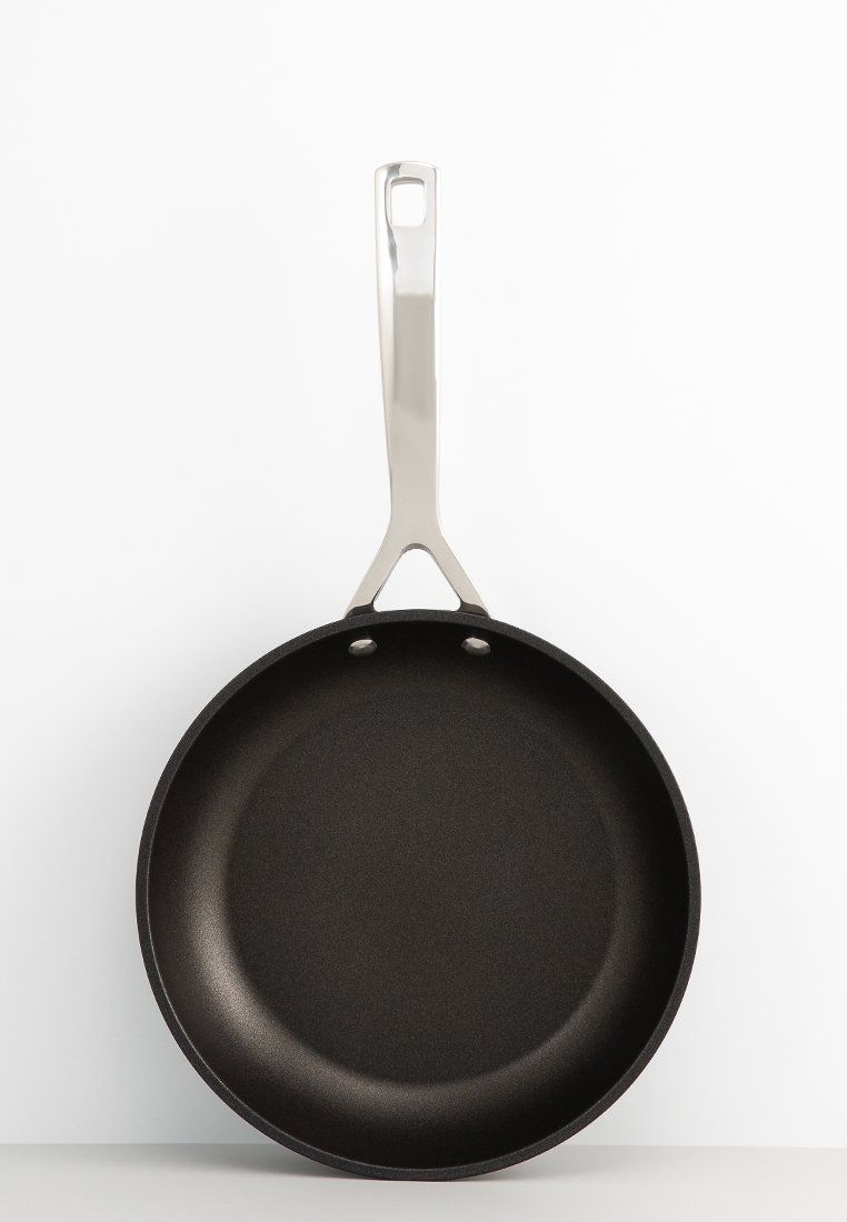 Patelnia nieprzywierająca o matowej czarnej powierzchni, zaokrąglonym kształcie i stalowym uchwycie z otworem do zawieszenia.