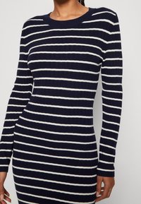 Stickad klänning med marinblå bas och vita vågräta ränder, med långt ärm och rund halsringning, samt ribbad textur.