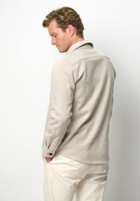 Giacca camicia a spina di pesce beige chiaro con colletto, maniche lunghe e polsini con bottoni, abbinata a pantaloni color crema. Texture liscia.