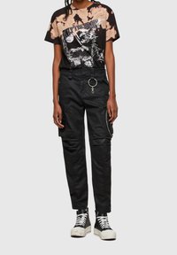 Černé tričko s ikatovým potiskem, doplněné černými cargo kalhotami se zipovými detaily, stříbrným prstýnkem a vysokými teniskami.