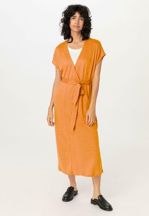 Kurzes oranges Wickelkleid mit kurzen Ärmeln, einem Bindegürtel in der Taille und lässigem Schnitt, kombiniert mit schwarzen Slippern.