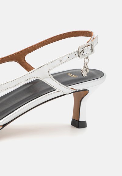 Witte leren hak sandaal met bruine accenten, verstelbare enkelband, zilveren hardware en een zwarte platform basis. Decoratieve charm inbegrepen.